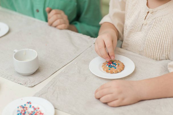 Cute children decorate cookies at a table in the home kitchen - Fotografie, Obrázek