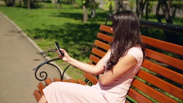Summer. A young girl in a pink dress is sitting on a bench in the park - Filmmaterial, Video