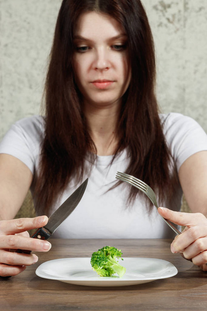sad young brunette woman dealing with anorexia nervosa or bulimia having small green vegetable on plate. Dieting problems, eating disorder. - Foto, Imagem