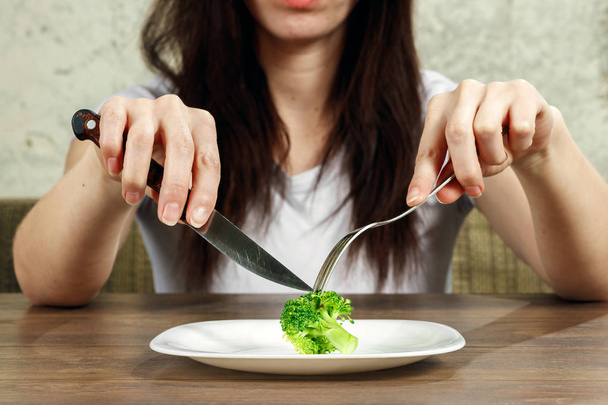 sad young brunette woman dealing with anorexia nervosa or bulimia having small green vegetable on plate. Dieting problems, eating disorder. - Фото, изображение