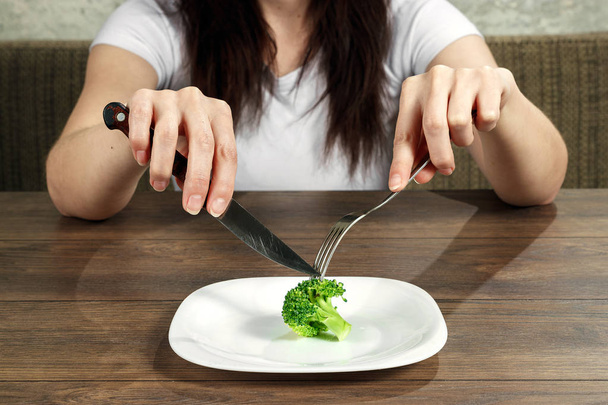 sad young brunette woman dealing with anorexia nervosa or bulimia having small green vegetable on plate. Dieting problems, eating disorder. - Фото, зображення