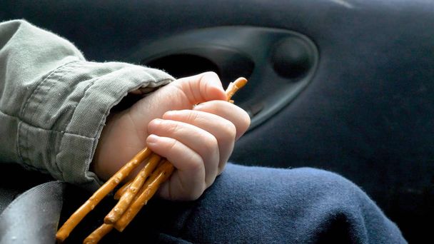 Вид крупным планом на детскую руку, держащую и поедающую печенье во время путешествия в машине
 - Фото, изображение