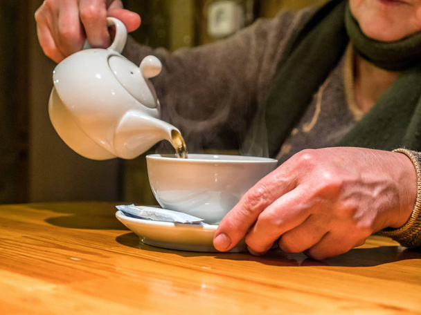 Lähikuva näkymä teekannu kaatamalla juoma kuppi senioreissa käsissä
 - Valokuva, kuva