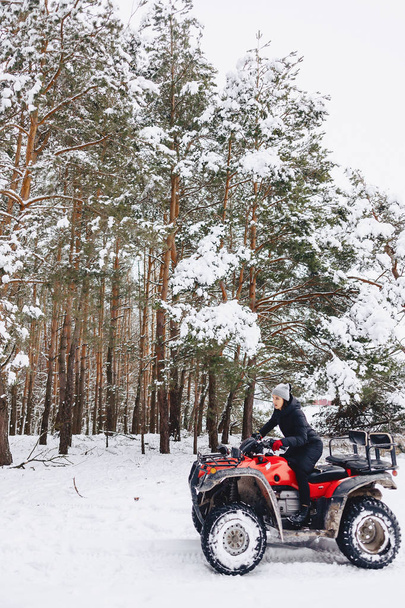 young girl on a motorcycle rides in snow-covered pine forest in  - Photo, Image