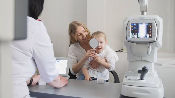 Оптометр перевіряє зір дитини - мати і дитина в кімнаті офтальмолога
 - Фото, зображення