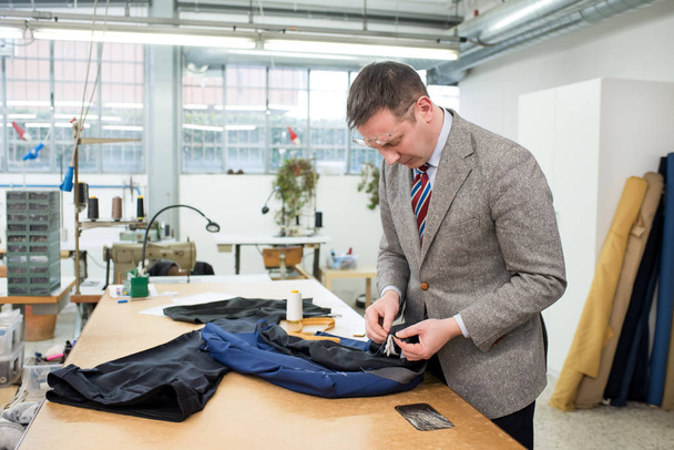 Tailor hand sewing the lining in a blue jacket - Foto, imagen
