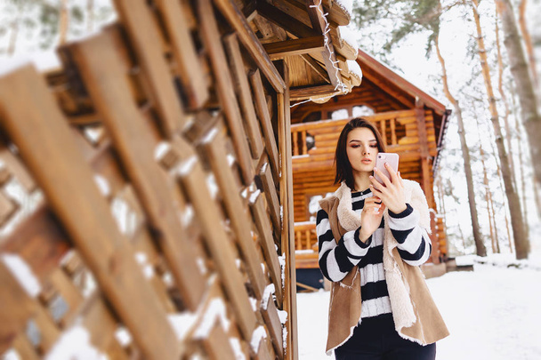 Młoda dziewczyna z telefonu w kamizelki na przeciwko drewniany domek  - Zdjęcie, obraz