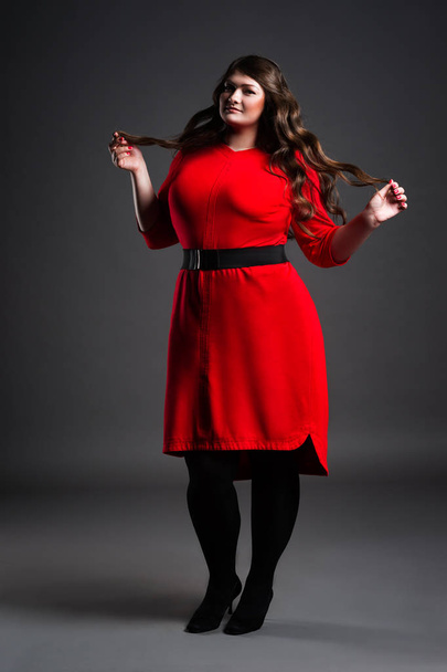 Plus size fashion model in red dress, fat woman on gray background, overweight female body - Valokuva, kuva