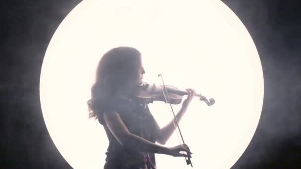 少女ミュージシャンのシルエット。バイオリニストは、白い円に対して煙でヴァイオリンを演奏します。. - 映像、動画