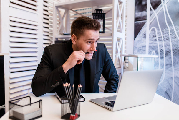 Businessman working behind a laptop, surprised and holding a pencil in his mouth.. - Valokuva, kuva