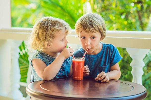 Children boy and girl drink orange smoothie from papaya. - Zdjęcie, obraz