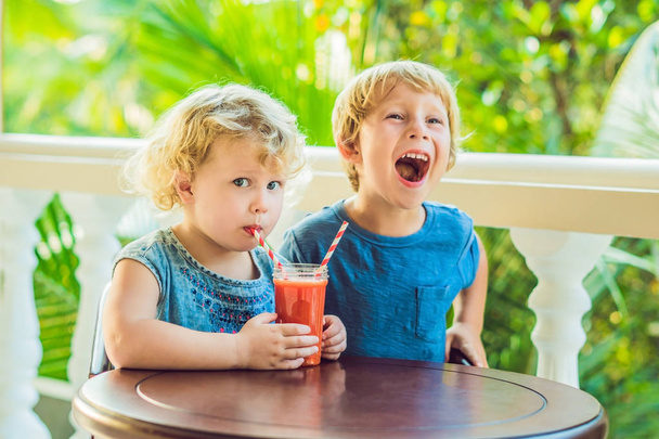 Children boy and girl drink orange smoothie from papaya. - Photo, Image