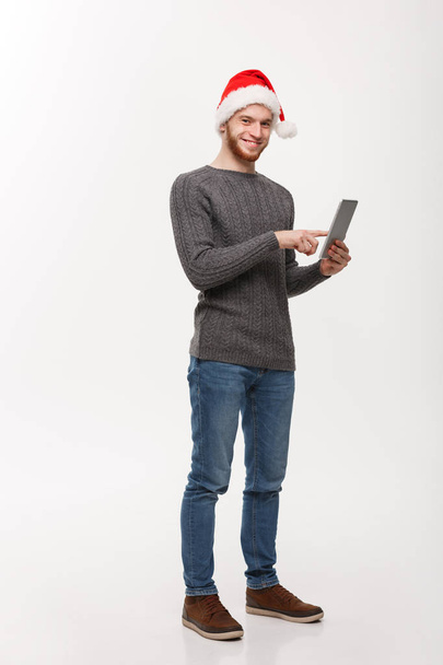 Holiday concept - Νεαρός γενειάδα όμορφος άντρας που εργάζεται σε ψηφιακή ταμπλέτα σε λευκό φόντο. - Φωτογραφία, εικόνα