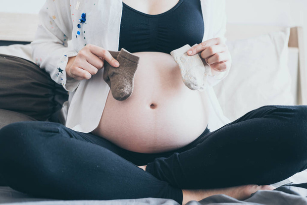 Ventre de la femme enceinte avec les mains en choisissant des chaussettes bébé
 - Photo, image