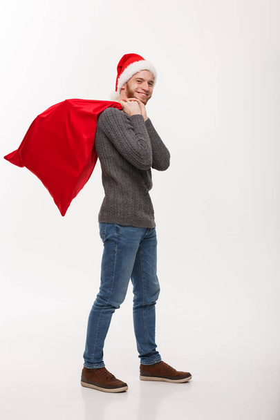 Weihnachtskonzept - junger selbstbewusster smarter Mann mit roter Weihnachtsmanntasche und vielen Geschenken im Inneren. - Foto, Bild