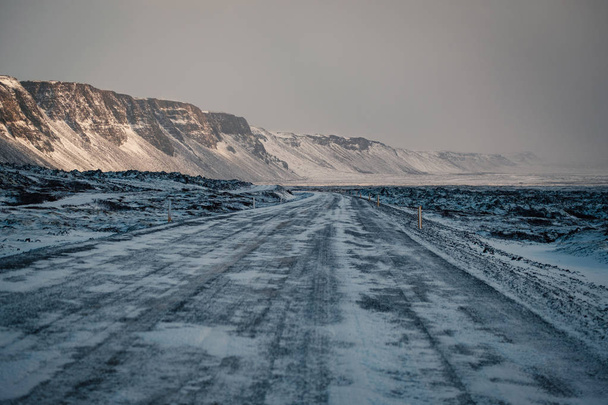 Winter road in snow blizzard. Blowing snow across the road. Difficult driving conditions in winter season in Iceland. Sunny but windy day, typical Icelandic route troubles. Icelandic safety driving. - Foto, Imagem