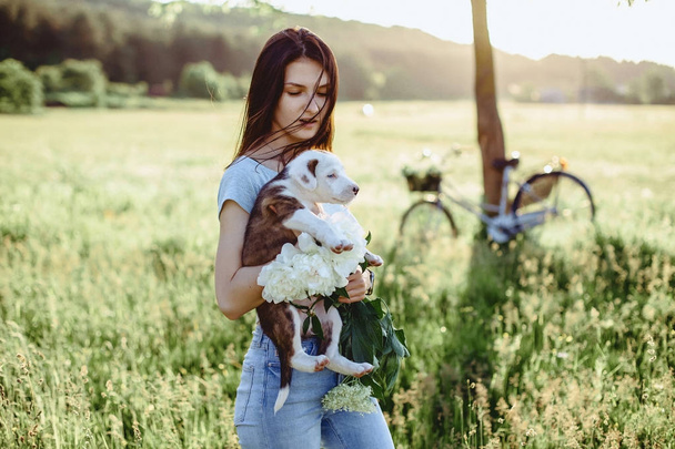 Девушка ходит с щенком в поле на велосипеде сзади
  - Фото, изображение