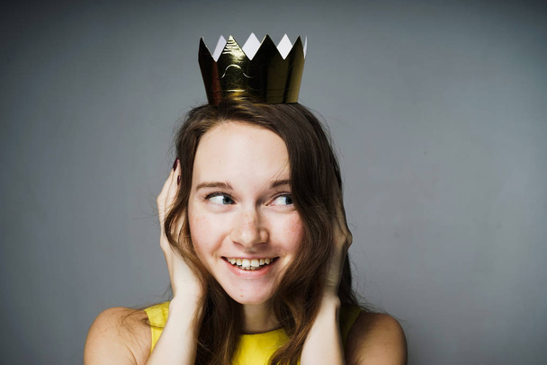 happy smiling girl in a yellow dress closed her ears with her hands, on her head a golden crown - Foto, afbeelding
