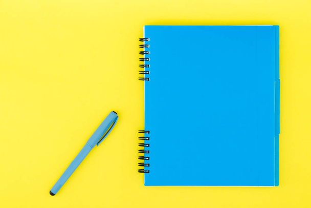 Een blauwe notebook met een handvat op een gele achtergrond. Plat lag sjabloon. Plaats voor tekst - Foto, afbeelding