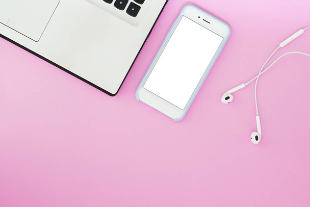 ein Telefon mit weißem Bildschirm, Laptop und Kopfhörer auf rosa Hintergrund und mit einem Platz für Text. flache Aufteilung der Geräte - Foto, Bild