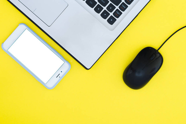 Smartphone en laptop met een muis op een gele achtergrond. Bovenaanzicht. Plat leggen. - Foto, afbeelding