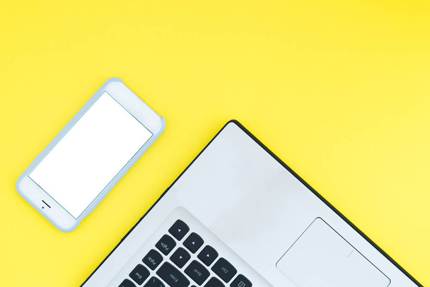 Un portátil y un smartphone con pantalla blanca sobre fondo amarillo. Espacio de trabajo minimalista con lugar para el texto. Piso Lay
 - Foto, Imagen