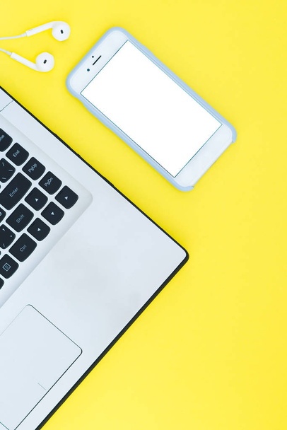 Laptop e smartphone com uma tela branca e fones de ouvido no fundo amarelo. Espaço de trabalho minimalista com um lugar para texto. Colocação plana
 - Foto, Imagem