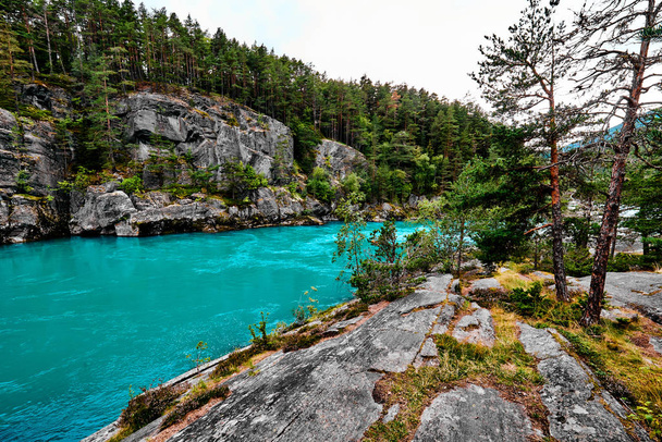 Изображение красивой плавающей бирюзовой реки в Норвегии. На заднем плане - берег, большие скалы и деревья
. - Фото, изображение