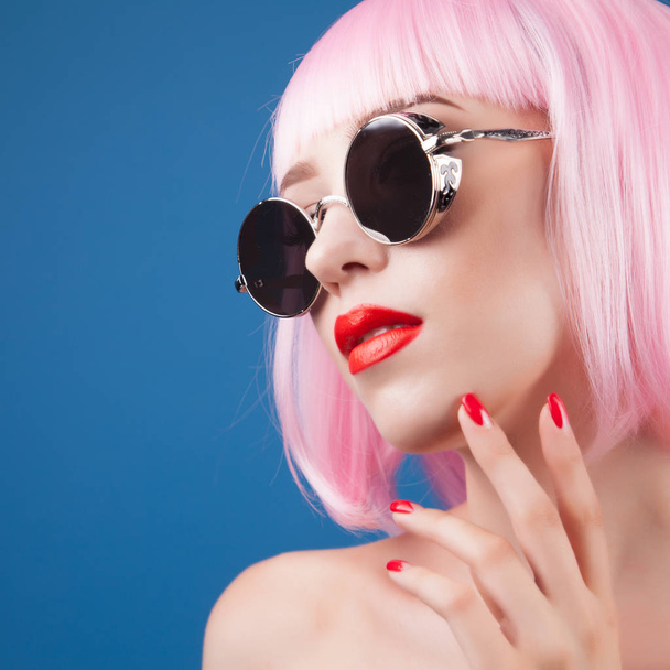 beautiful woman wearing colorful wig and silver sunglasses against blue background - Foto, immagini