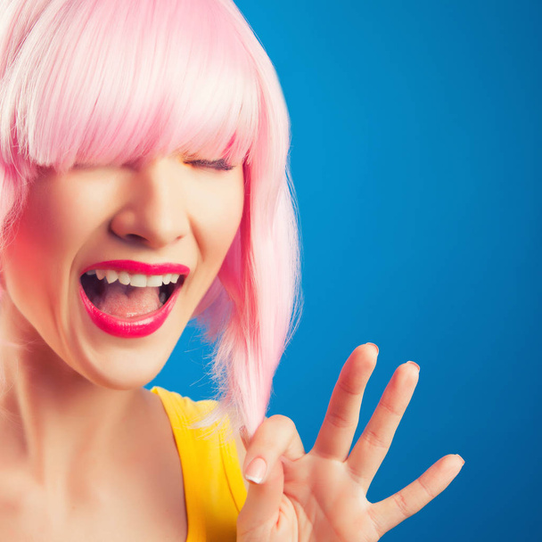 beautiful woman wearing pink wig against blue background - Foto, Bild