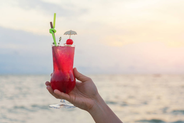 Bebida de cóctel roja de mano en el crepúsculo fondo del mar y el cielo
 - Foto, Imagen