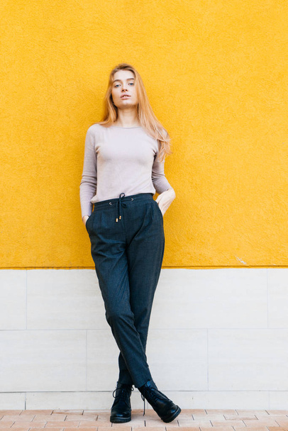 slim stylish beautiful blonde girl posing against a yellow wall background, street fashion and style - Photo, image