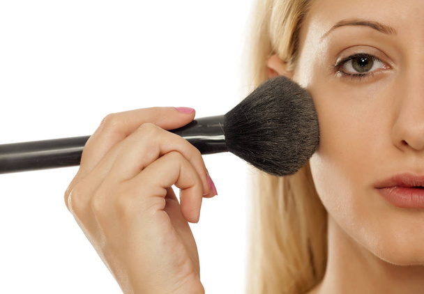 Young blonde woman applying powder on her face with makeup brush - Fotó, kép