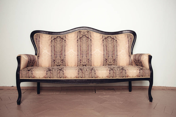 Lujoso sofá de terciopelo antiguo se encuentra en un suelo de madera cerca de la pared
 - Foto, imagen