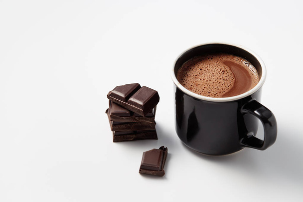 Black mug with hot chocolate served with chunks of dark chocolate  - Фото, изображение