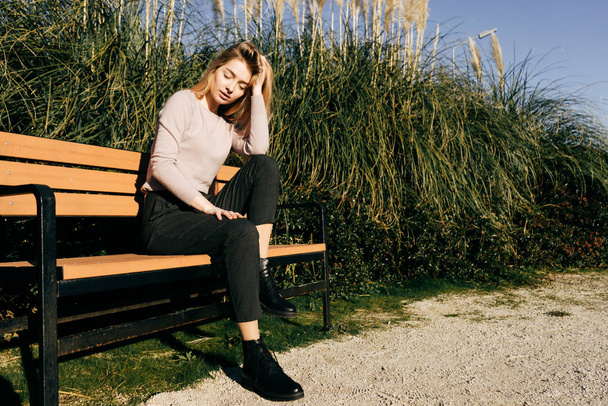 stylische junge blonde Mädchen sitzt auf einer Bank im Freien, in der Sonne, schloss die Augen - Foto, Bild