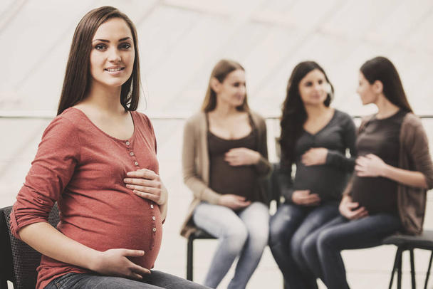 Beautiful pregnant woman is looking at the camera. Happy pregnant women are talking together at antenatal class at the hospital on background - 写真・画像