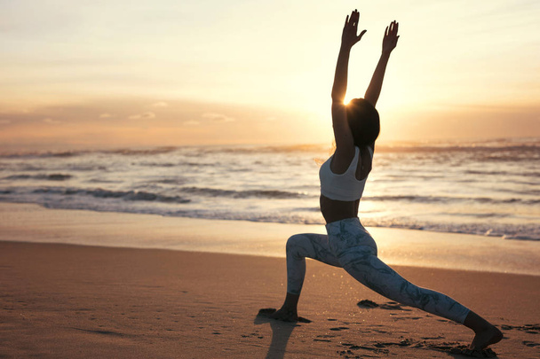 Silhouet van sportieve jonge vrouw doen yoga praktijk op strand, begrip van gezond leven en natuurlijke evenwicht tussen lichaam en geestelijke ontwikkeling - Foto, afbeelding