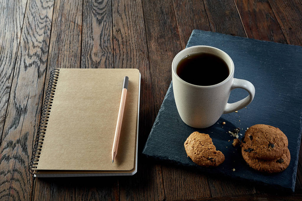 Cup of tea with cookies, workbook and a pencil on a wooden background, top view - Foto, Imagen