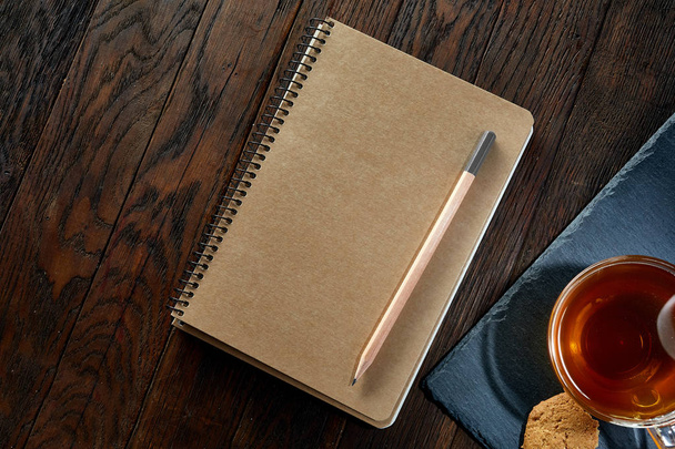 Cup of tea with cookies, workbook and a pencil on a wooden background, top view - Фото, зображення