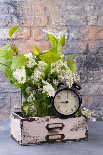Alarm clock with spring blooming branch in wooden drawer against brick wall background. - Photo, Image