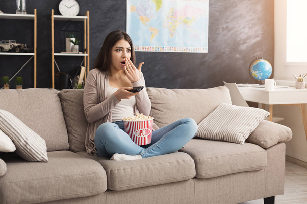 Молода жінка сидить на дивані і дивиться телевізор
 - Фото, зображення