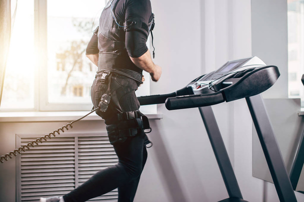 Muž v černém obleku pro ems trénink, běh na běžeckém pásu v posilovně - Fotografie, Obrázek