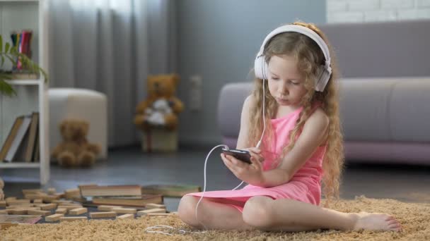 Kid in headphones listening to music on smartphone, addicted to technology - Кадри, відео