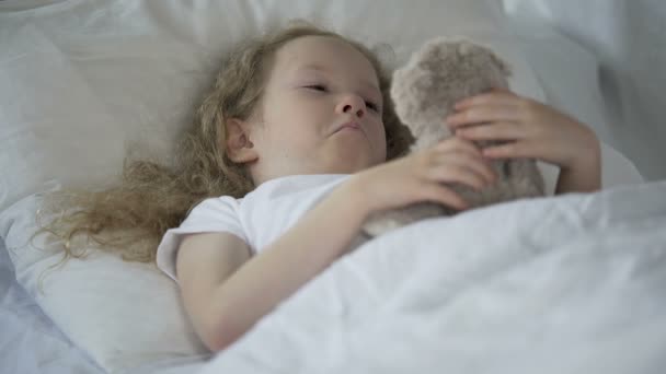 Lonely young girl lying in bed and hugging toy, unhappy child missing parents - Materiał filmowy, wideo