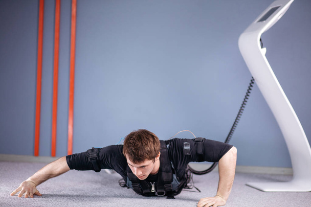 EMS male doing push ups in gym while connected to electric muscle stimulator - Foto, imagen