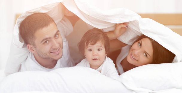 Happy family posing under a duvet while looking at the camera - Foto, Bild
