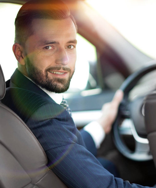 бизнесмен, сидящий за рулем автомобиля и смотрящий в камеру
 - Фото, изображение