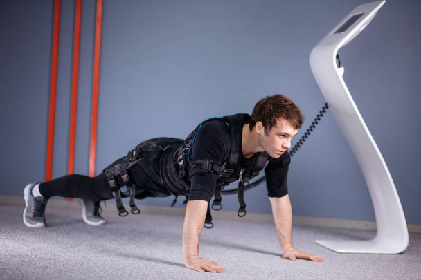 человек в электрических мышечных стимуляционных костюмах делает упражнения на доске. EMS
 - Фото, изображение