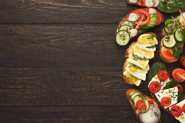 Разнообразие здоровых вегетарианских бутербродов на темной древесине, вид сверху
 - Фото, изображение